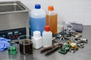 cuba de ultrasonidos con botellas de detergente y piezas metalicas en mesa de trabajo industrial sin texto en imagen